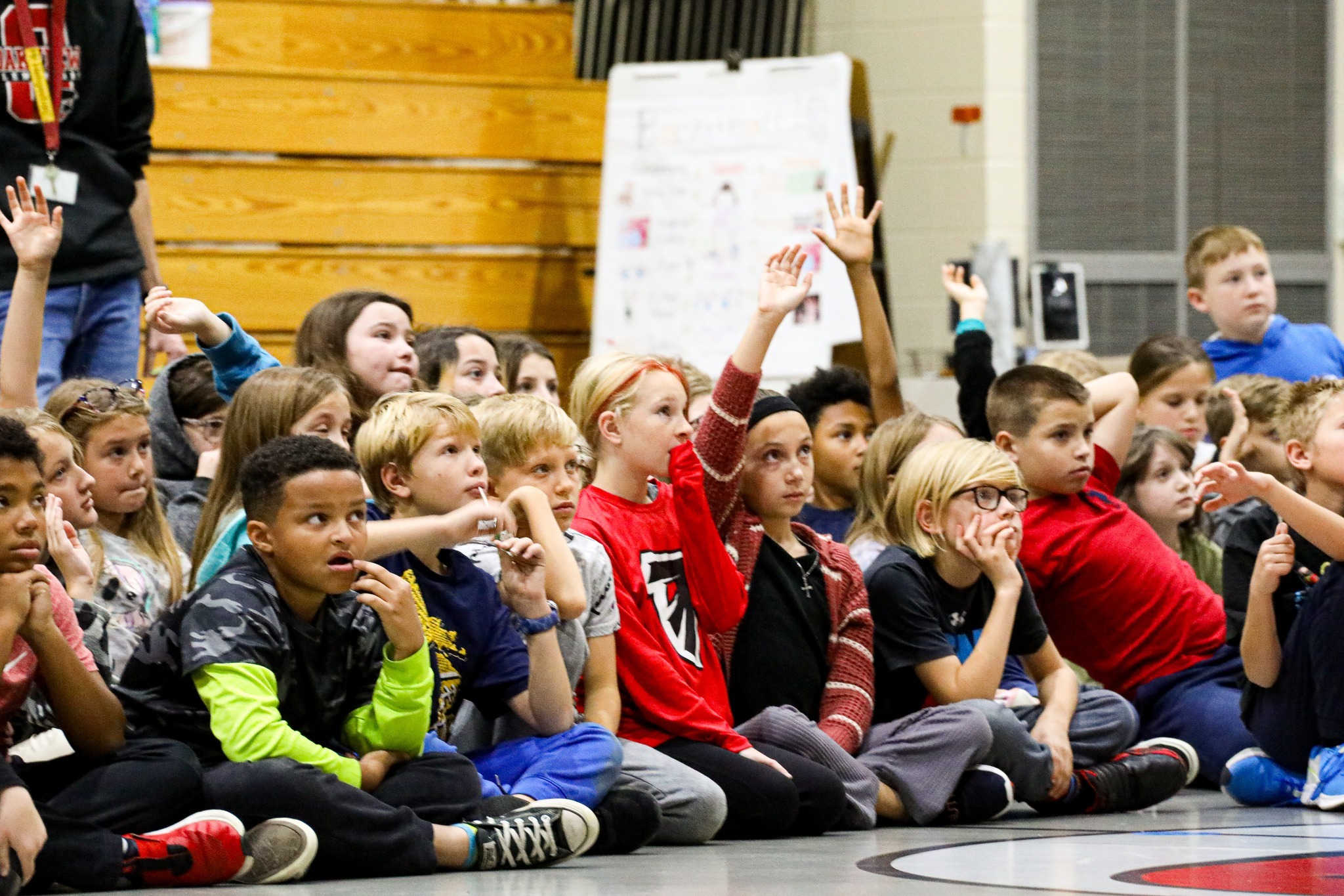 Kids on gymnasium floor raising hands to participate in discussion